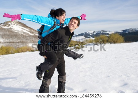Playful couple having fun on winter hiking trip to mountain. Man and woman enjoying freedom playing around and laughing on snow.