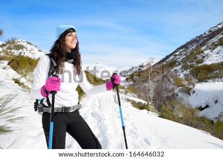 Woman hiking on sunny winter day in mountain landscape. Female hiker in warm outfit enjoying trail walk on snow covered track.