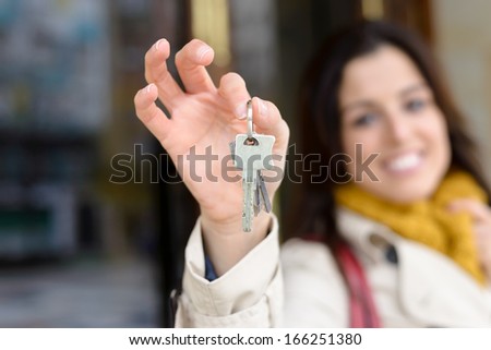 Woman holding home keys outside from apartment building. Rental, insurance or ownership concept.