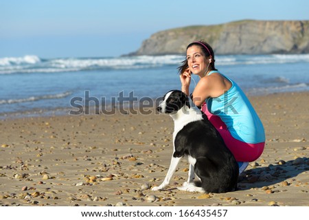 Joyful fitness woman with dog on beach taking a break from running. Sporty girl with her pet on summer sport  and relaxing day.