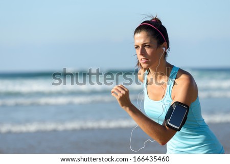 Fitness Woman Running On Beach While Listening Music. Sporty Girl Wearing Arm Sport Band For Smartphone.