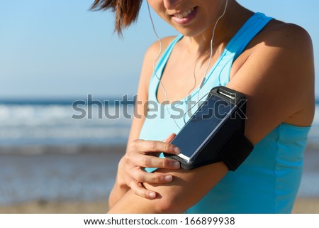 Sporty Woman Touching Phone Screen In Arm Sport Band Before Running On Beach. Female Athlete Listening Music While Doing Sport.