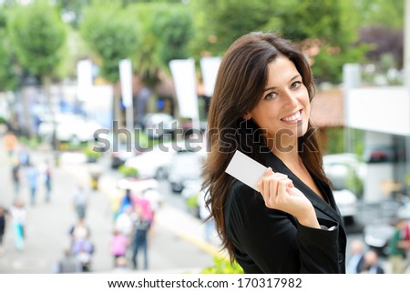 Successful female car sales representative showing business card  in automobile trade fair. Beautiful brunette saleswoman outdoor.