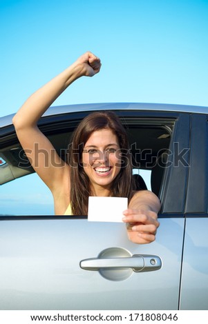 Female young car driver after passing the driving license test. Successful woman showing blank card and smiling in vehicle.