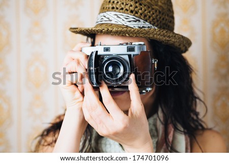 Hipster woman taking photos with retro film camera on vintage ornamental wallpaper.