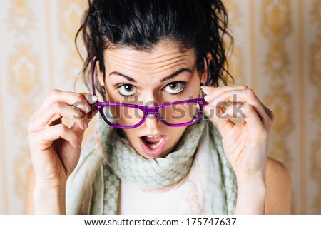 Surprised woman looking over her glasses. Beautiful jaw dropped girl with modern eyewear.