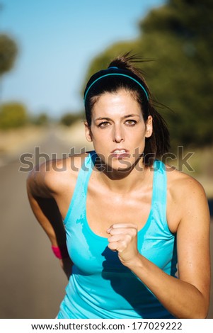 Sweaty female athlete running on road. Fitness woman training and exercising hard.