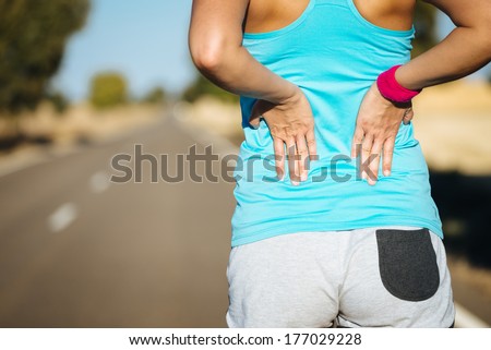 Female runner athlete back injury and pain. Woman suffering from painful lumbago or kidney illness while running in rural road.