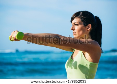 Fitness woman on workout. Motivated girl working out with dumbbells outdoor.