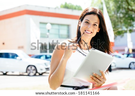 Successful female car sales consultant in business trade fair showing blank digital tablet screen and approving with thumbs up. Vehicle offer and information concept.