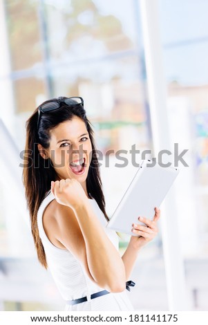 Digital business success in internet concept. Successful woman celebrating achievement with digital tablet indoor.