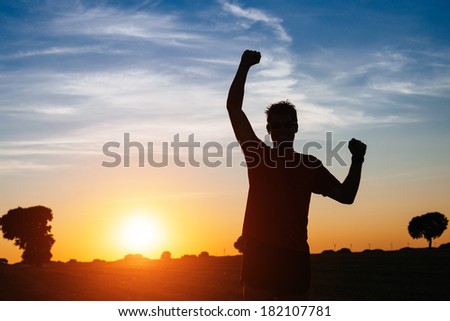 Successful man raising arms after cross country running on summer at sunset. Male athlete with arms up celebrating success and sport goals after exercising and working out.