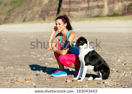 Relaxed fitness woman with dog listening music with sport arm band and earphones at the beach. Sporty girl taking a breath before running.