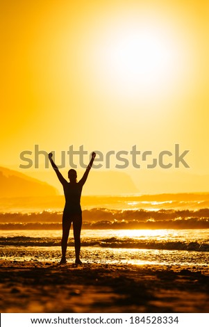 Fitness woman celebrating sport success on beautiful summer sunset or sunrise on the beach.  Successful female runner silhouette raising arms to the sun.