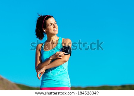 Happy fitness woman wearing sport smartphone armband and earphones listening music before running and exercising on summer.
