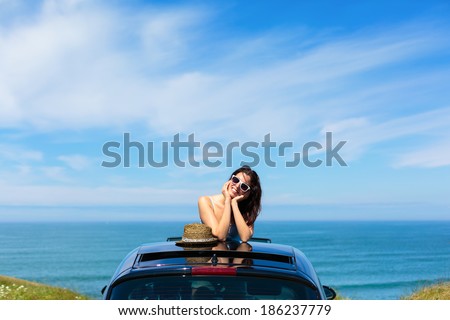 Relaxed tranquil woman on summer travel vacation to the coast  leaning out car sunroof with the sea on background.