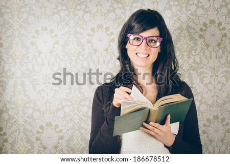 Happy woman reading old book and turning the page on floral decorated wall background. Instagram retro filtered image.