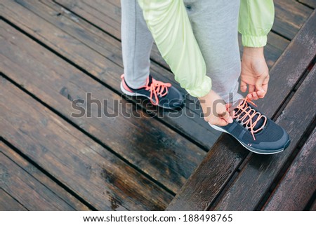 Fitness woman lacing running sport shoes before workout on rainy day.