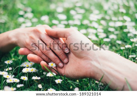 Young romantic  lovers holding hands gently on spring flowers field. Love and affection concept.