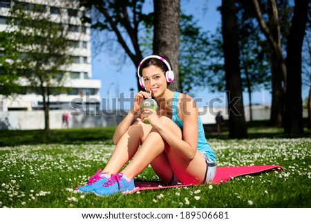 Relaxed fitness woman on a workout rest drinking detox smoothie on spring or summer. Beautiful fit girl taking a rest in city park.