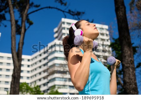 Fitness woman working out with dumbbells in city park. Spring or summer exercising workout with weights. Urban sport lifestyle concept.