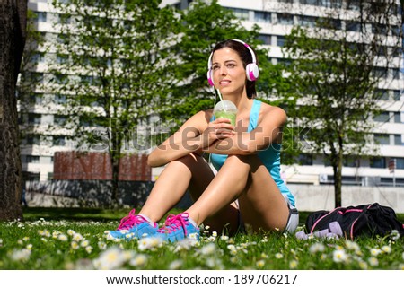 Relaxed fitness woman on a workout rest drinking detox smoothie on spring or summer. Beautiful fit girl taking a rest in city park.