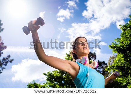 Fitness woman working out with dumbbells in city park. Spring or summer exercising workout with weights. Urban sport lifestyle concept.