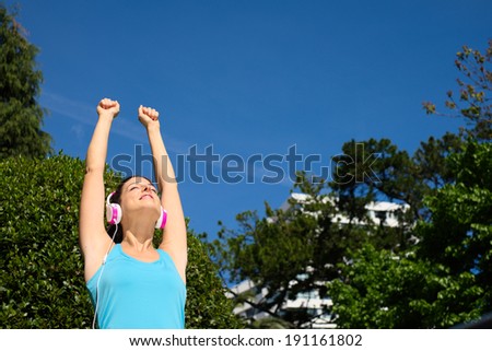 Fitness success concept. Successful sporty girl raising arms in city park after workout.