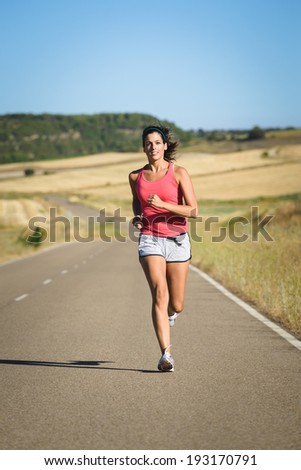 Female fit athlete on running workout in country road . Sporty powerful woman exercising on summer.