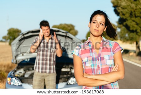 Upset woman waiting for car help while man arguing on the cellphone with insurance service. Couple in road trip problems because of breakdown engine.
