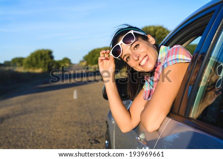 Cheerful woman on summer car travel. Female driver on roadtrip looking at camera and smiling.