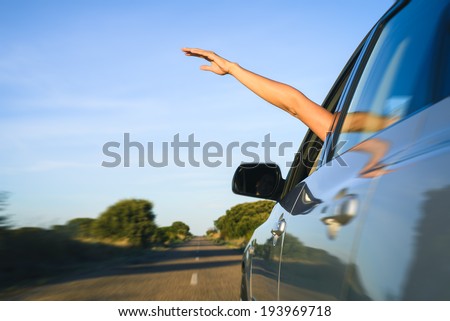 Woman sticking arm out of the car window on roadtrip. Female driver hand feeling the air and freedom.