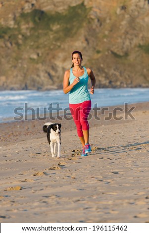 Fitness woman with dog running and exercising at beach on summer. Brunette female athlete training with her pet.