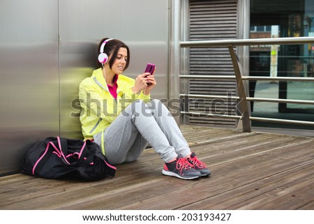 Cheerful female athlete texting message or email on smartphone on a urban fitness workout break. Sporty woman looking her cellphone.