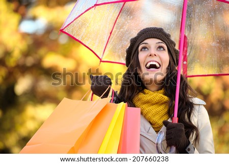Happy woman holding shopping bags and umbrella under autumn rain. Brunette fashion female shopper outside in fall season.