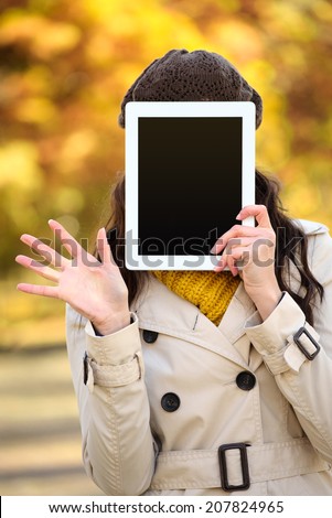 Unrecognizable woman covering her face with digital tablet blank screen and waving in autumn season. Hidden female holding touchpad frame for copy space message or information.
