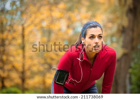 Tired female runner taking a break. Sporty woman breathing and resting on running training in autumn.