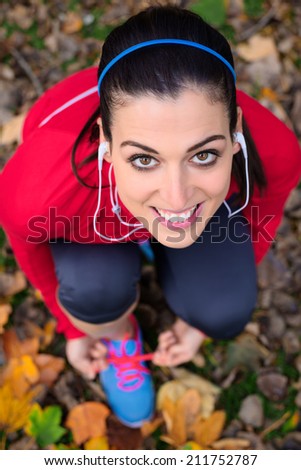 Happy female athlete getting ready for running outdoor in autumn. Sporty woman lacing sport shoes.