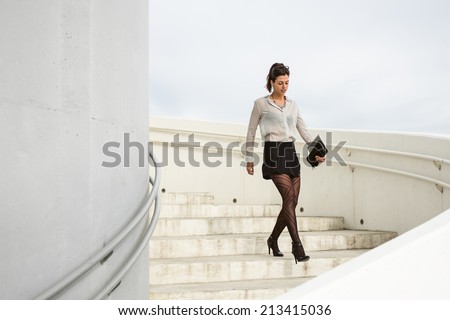 Trendy young businesswoman walking down the stairs of corporate building on a working day. Brunette professional woman wearing sexy skirt and stockings.