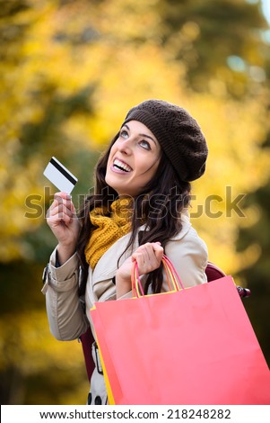 Fashion trendy woman showing credit card and carrying shopping bags after buying in autumn. Happy caucasian brunette shopper spending money.