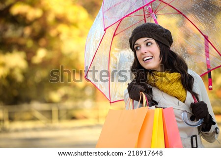 Happy young woman with shopping bags and umbrella in autumn rainy day. Fashion female shopper outside.