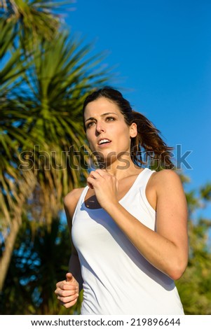 Female athlete running outdoor in a park on summer. Brunette woman training and exercising.