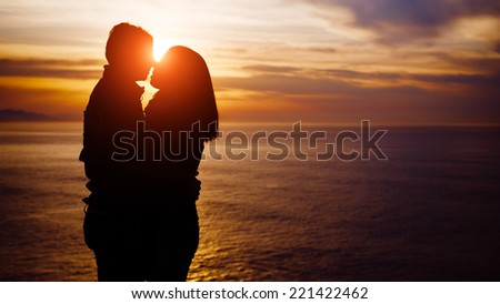 Young couple kissing on beautiful romantic sunset towards the sea. Love and romance concept.