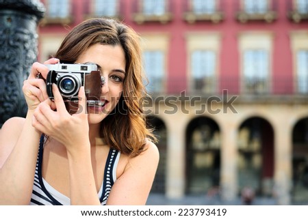 Woman taking photo with retro camera in Gijon Main Square, Asturias, Spain. Female tourist visiting typical spanish landmark on summer vacation travel.