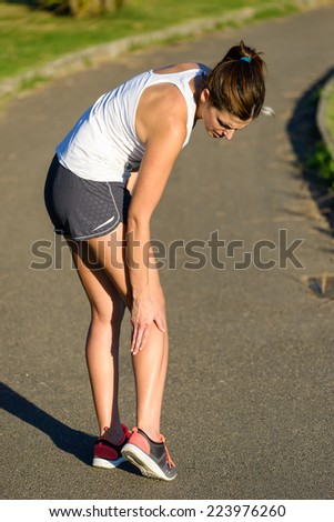 Female caucasian athlete suffering a calf muscle cramp injury while running outdoor in a park.