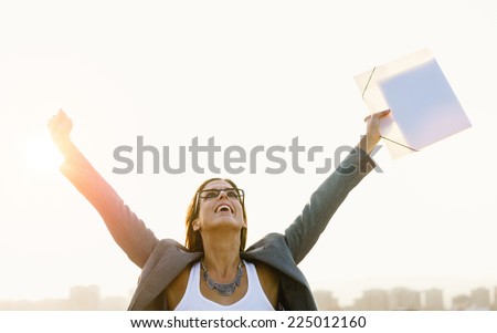 Successful young businesswoman with arms up celebrating business  or job success towards city skyline on sunset or sunrise. Professional happy woman outside.
