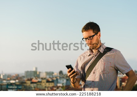 Professional casual man messaging or checking his smartphone against city background.