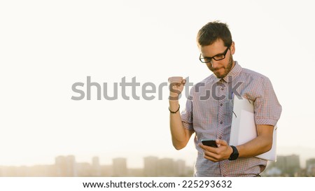Successful professional casual man gesturing and checking cellphone messages towards city skyline. Entrepreneur enjoys success in job.