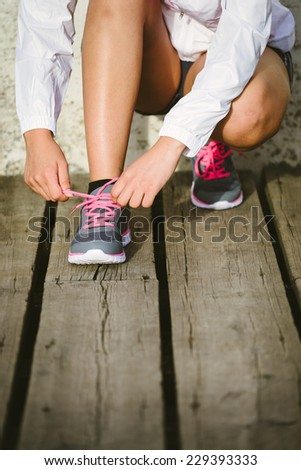 Female caucasian athlete getting ready for running training. Woman tying sport footwear laces. Sport and healthy lifestyle concept.