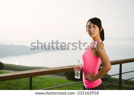 Motivated female athlete taking a workout break for drinking water. Asian woman on a training rest towards the sea.